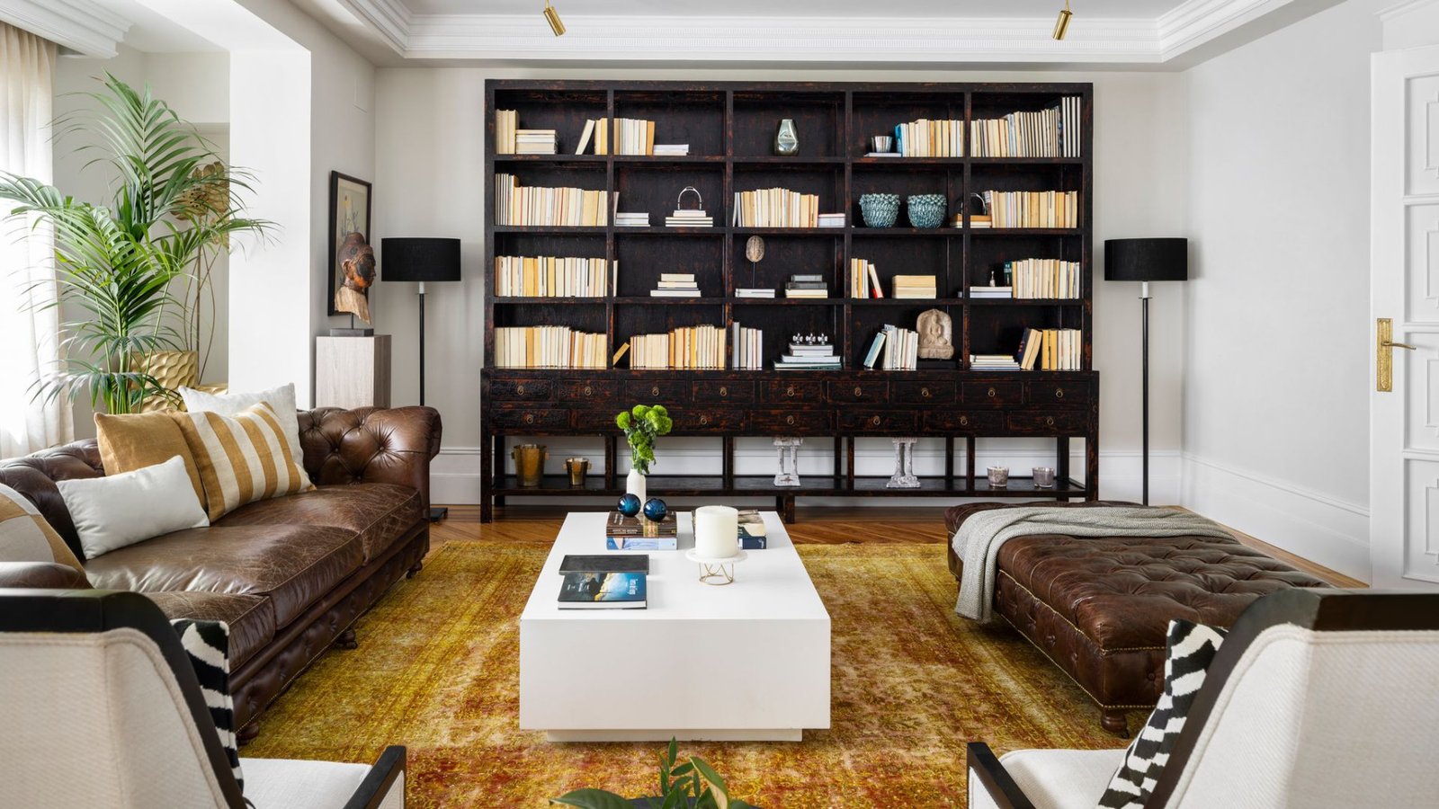 Library in a Spanish home with floor-to-ceiling shelves, leather and soft greenery