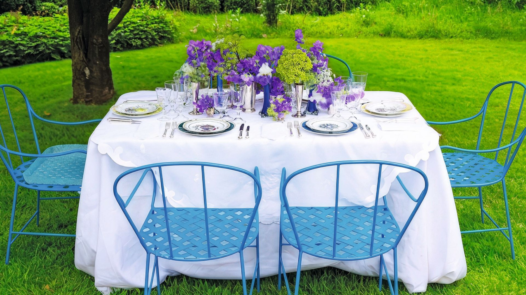 A lunch table in the garden with blue chairs and purple flowers
